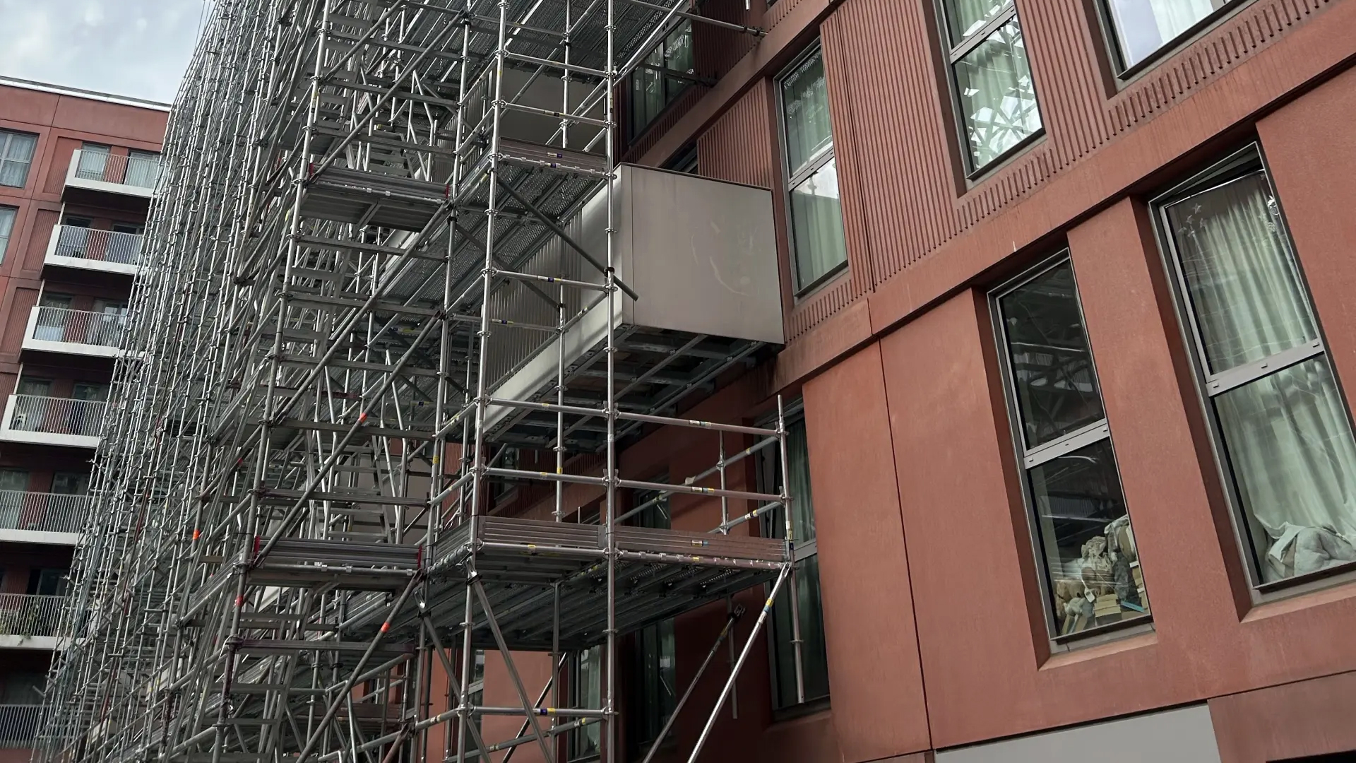 A high rise building with a red façade and scaffolding used to remediate the outside