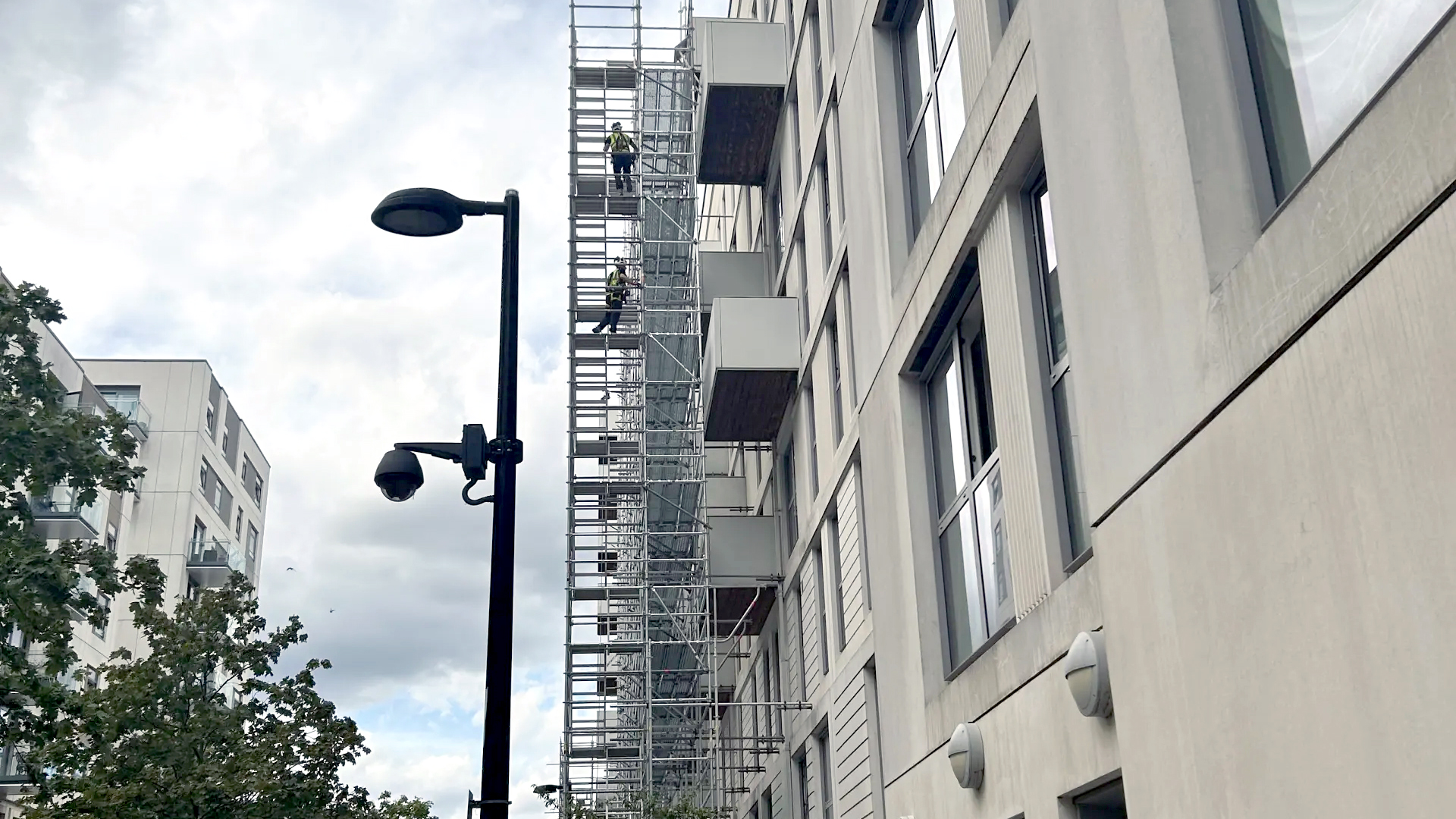 A high rise building with a grey façade and scaffolding with workers remediating the outside